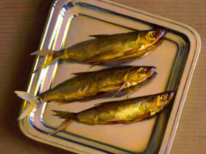 Three golden-yellow fish, a creation by the Duluth MN artist, are placed on a reflective metal tray against a brown table surface. The fish, arranged side by side, boast glistening scales and visible fins. The lighting gives them a shiny, lustrous appearance.