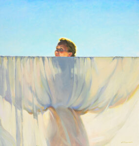 A Duluth MN artist stands behind a large billowing white cloth under a clear blue sky, with only their face visible above the fabric. Soft sunlight highlights the scene, creating a serene and airy atmosphere.