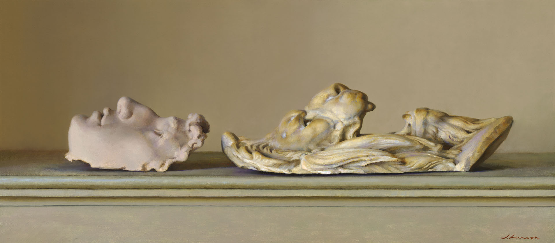 Two classical-style sculptures rest on a surface. On the left, a serene face with curly hair is depicted; on the right, an intricate relief showcases multiple faces intertwined in a dynamic composition. Created by a talented Duluth MN artist, both pieces are set against a neutral background.