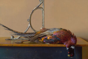 A still life painting by a Duluth MN artist depicts a colorful pheasant lying on its side atop a wooden table. The bird's plumage features rich hues of red, green, and purple. In the background, a decorative metal bracket contrasts with the plain wall.