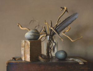 A still life by a Duluth MN artist features a jar with twisted branches and a large feather, a wooden block with a striped round object on top, a small empty nest, and a smooth dark sphere placed on a rustic table.