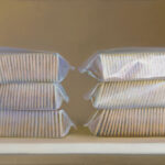 Six stacks of packaged golden crackers, reminiscent of a Duluth MN artist's palette, are neatly arranged in rows of three on a shelf, set against a plain neutral background. The packaging is slightly glossy, reflecting light softly.