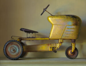 A vintage yellow toy tractor, crafted by a Duluth MN artist, features worn paint and a single steering wheel. Displayed against a plain background, the nostalgic design includes a simple seat and three wheels.