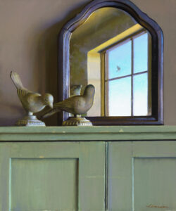 A wooden cabinet crafted by a Duluth MN artist showcases two bird sculptures in front of an arched mirror. The mirror reflects a window revealing a bright blue sky and a small bird in flight outside. The scene is calm and softly lit.