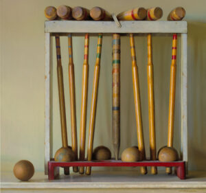 A wooden rack, crafted by a talented Duluth MN artist, holds an assorted set of vintage croquet mallets and balls. The mallets boast colorful stripes, while the frame is painted white. A red base supports the structure against a neutral background.