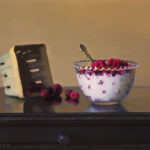 A still life painting by a Duluth MN artist features a wooden table adorned with a decorative bowl brimming with raspberries and a silver spoon. Nearby, an empty wooden basket rests, with scattered raspberries beside it against the backdrop of a plain beige wall.