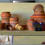 A collection of stacked and scattered terracotta pots sit on a shelf, crafted by a talented Duluth MN artist. Accompanied by a spool of twine and folded towel, a small black pot holds purple flowers, adding a touch of color to the earthy scene.