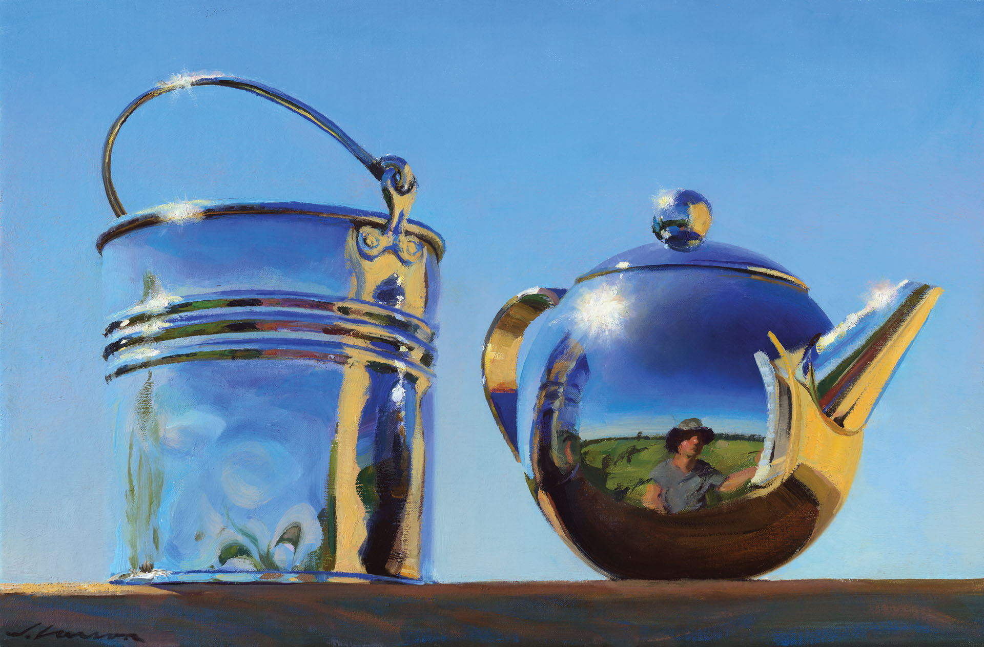 A reflective silver teapot crafted by a Duluth MN artist and a metal bucket sit on a wooden surface under a clear blue sky. The teapot's surface captures the distorted reflection of the landscape and a person taking the photo.