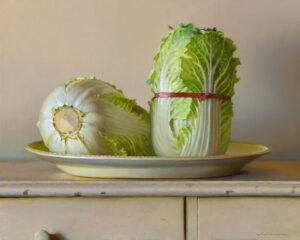 A realistic painting by a Duluth, MN artist depicts two heads of cabbage on a plate. One cabbage is upright, bound with a red band, while the other lies on its side, exposing the stem. The composition rests on a wooden surface against a neutral background.