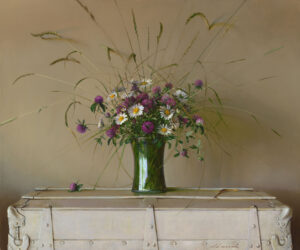 A bouquet of purple and white flowers with long grasses, arranged by a talented Duluth MN artist in a green glass vase, sits elegantly atop a cream-colored trunk against a beige background.