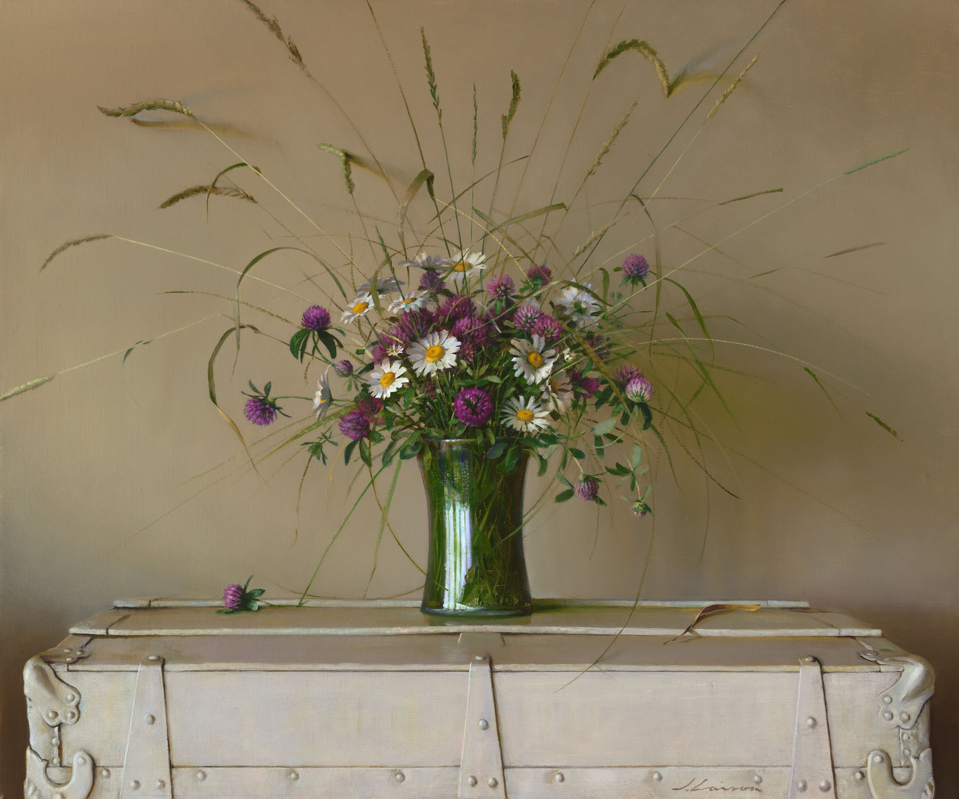 A bouquet of purple and white flowers with long grasses, arranged by a talented Duluth MN artist in a green glass vase, sits elegantly atop a cream-colored trunk against a beige background.