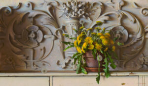 A clay pot filled with vibrant yellow dandelions, crafted by a talented Duluth MN artist, sits on a beige wooden shelf against an intricately carved decorative wall featuring floral patterns and ornate designs.