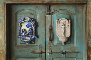 A rustic green door, crafted by a talented Duluth MN artist, features two ornate decorations: a blue and white ceramic plaque on the left, depicting a scene with figures, and a beige bas-relief on the right, showcasing a crucifix design.