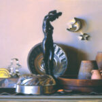 A collection of metallic kitchenware and decorative items by a Duluth MN artist is displayed on a shelf, featuring a black statue of a standing figure, moon and star cookie cutters, a gingerbread man mold, and various bowls and pots.