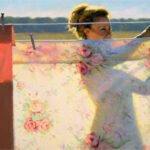 A Duluth MN artist hangs floral-patterned sheets on an outdoor clothesline. The scene is brightly lit by the sun, casting shadows on the fabric. In the background, a blurred landscape of fields unfurls under a clear sky.