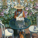 A Duluth MN artist in a straw hat sits at a blue metal table, sipping from a cup and reading a book. She is surrounded by blooming white flowers on a sunny day, creating a serene garden atmosphere.