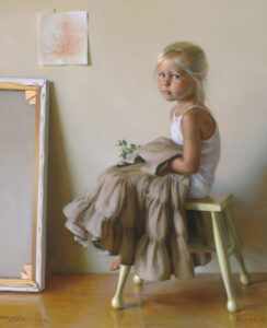 A young girl with blonde hair sits on a green stool, wearing a white top and a tan skirt. She holds fabric in her lap and looks toward the viewer. Behind her, a framed picture and a child's drawing hang, hinting at the playful creativity of a Duluth MN artist.