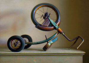 A vintage, rusted tricycle by a Duluth, MN artist is displayed upside down on a table, casting an intricate shadow on a plain background. The tricycle's worn paint and visible wear suggest age and use, with its handlebars and wheels prominently featured.