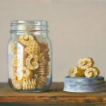 A glass jar filled with intricately shaped pasta, a creation by a talented Duluth MN artist, is placed on a wooden surface. The jar's lid lies beside it with a few pieces of pasta resting on top. The lighting casts soft shadows, creating a warm, inviting scene.