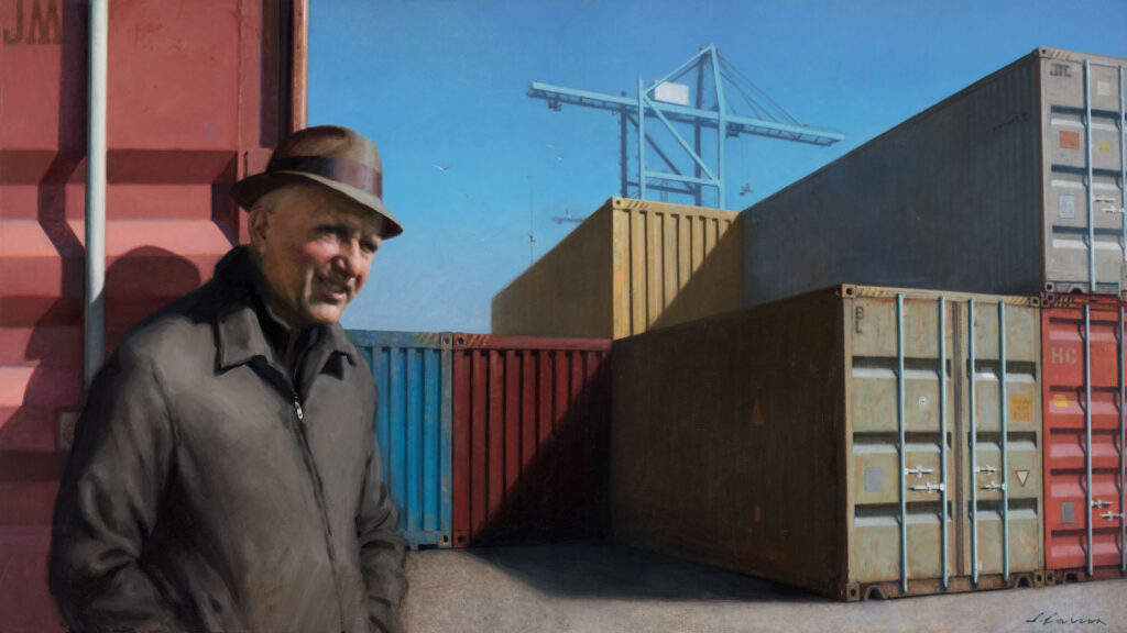 A man wearing a hat and coat stands in front of stacked shipping containers under a clear blue sky. Amid the industrial symphony, reminiscent of the rugged charm often captured by a Duluth MN artist, a crane rises majestically among the containers, suggesting the pulse of this bustling port.