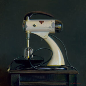 A vintage electric mixer with a white body and black accents sits on a dark wooden table against a dark background. Its cord is coiled on the table.