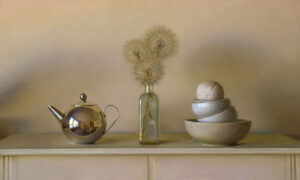 A polished silver teapot reflects its surroundings. Next to it, a glass bottle by a Duluth MN artist displays dried dandelions. Beside the bottle, three stacked bowls hold a ball of twine. All are arranged on a pale surface against a beige background.