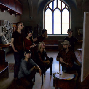 A group of seven people, some seated and some standing, are gathered in an art atelier. They are focused on a canvas while sunlight streams through a large arched window, reminiscent of a Minnesota morning. Art supplies and sculptures are scattered throughout the room.
