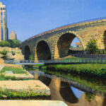A painting by a Duluth, MN artist captures a historic stone arch bridge spanning a calm river, its reflection shimmering on the water. Tall buildings rise against the clear blue sky while lush greenery lines the riverbanks, effortlessly blending nature with urban elegance.