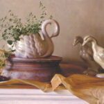 A still life by a Duluth MN artist depicts a white swan-shaped vase adorned with greenery, cherries, and two ceramic ducks on a brown and white surface. The neutral beige backdrop, complemented by rustic parchment, enhances the composition's charm.