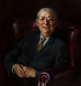 A portrait by a Duluth MN artist captures an older man in a dark leather armchair, dressed in a dark suit with a patterned tie and glasses. He smiles warmly, hands clasped in his lap. The dim background accentuates the subject's presence.