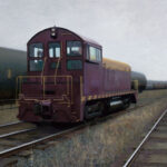 A maroon locomotive, resembling an evocative scene from a Duluth MN artist's canvas, travels along railway tracks next to a line of black tank cars. The sky is overcast, and the landscape is flat, with dry grass bordering the tracks.